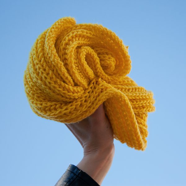 Handgestrickter gelber oversize Schal für Kinder der in die Luft gehalten wird. Bjarki
